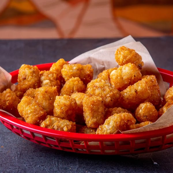 A red basket filled with crispy, golden-brown tater tots lined with parchment paper.