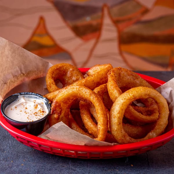 A red basket filled with crispy golden onion rings and a side of dipping sauce.