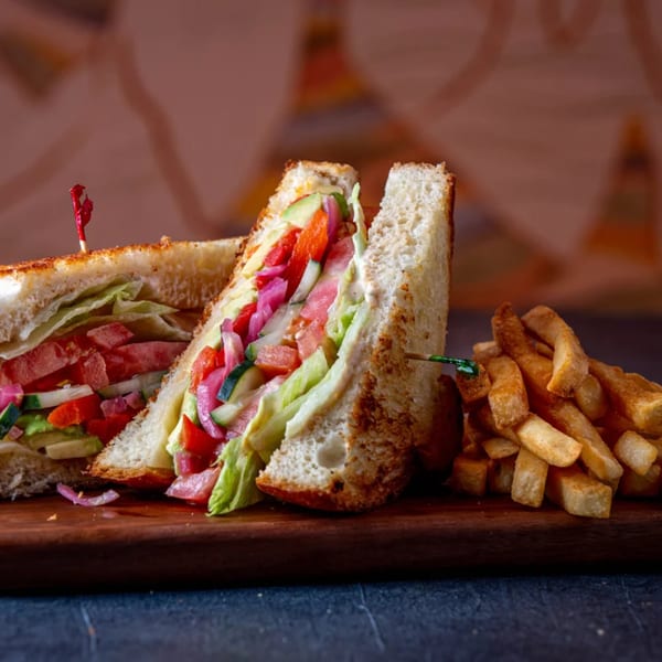 A toasted club sandwich with fresh vegetables and a side of golden french fries on a wooden board.