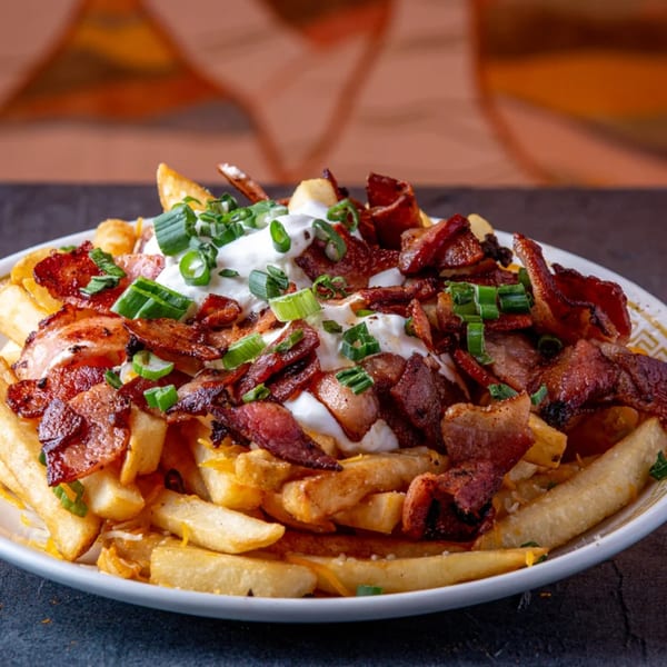 Dusty's Hideaway loaded fries with crispy bacon, sour cream, and green onions on a white plate.