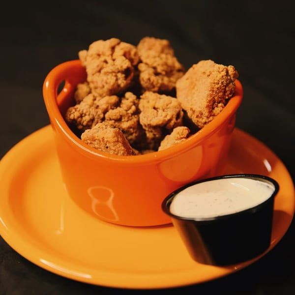 Crispy fried chicken bites in an orange bowl with a side of ranch dressing.